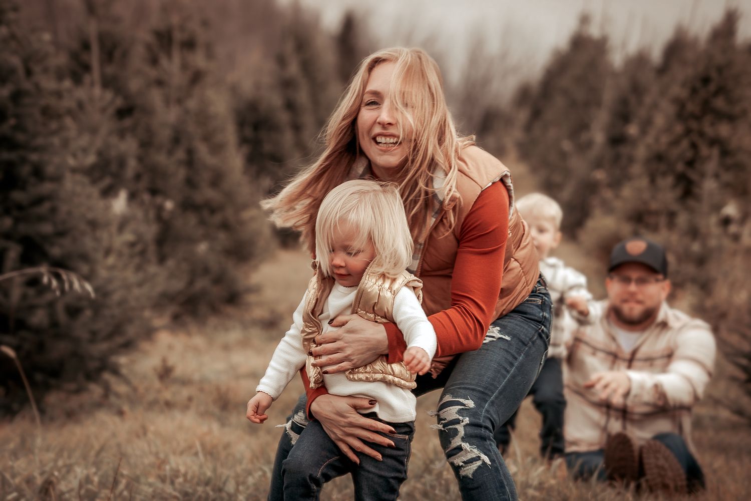 Family enjoying a playful autumn photoshoot together among evergreen trees in a natural outdoor setting.