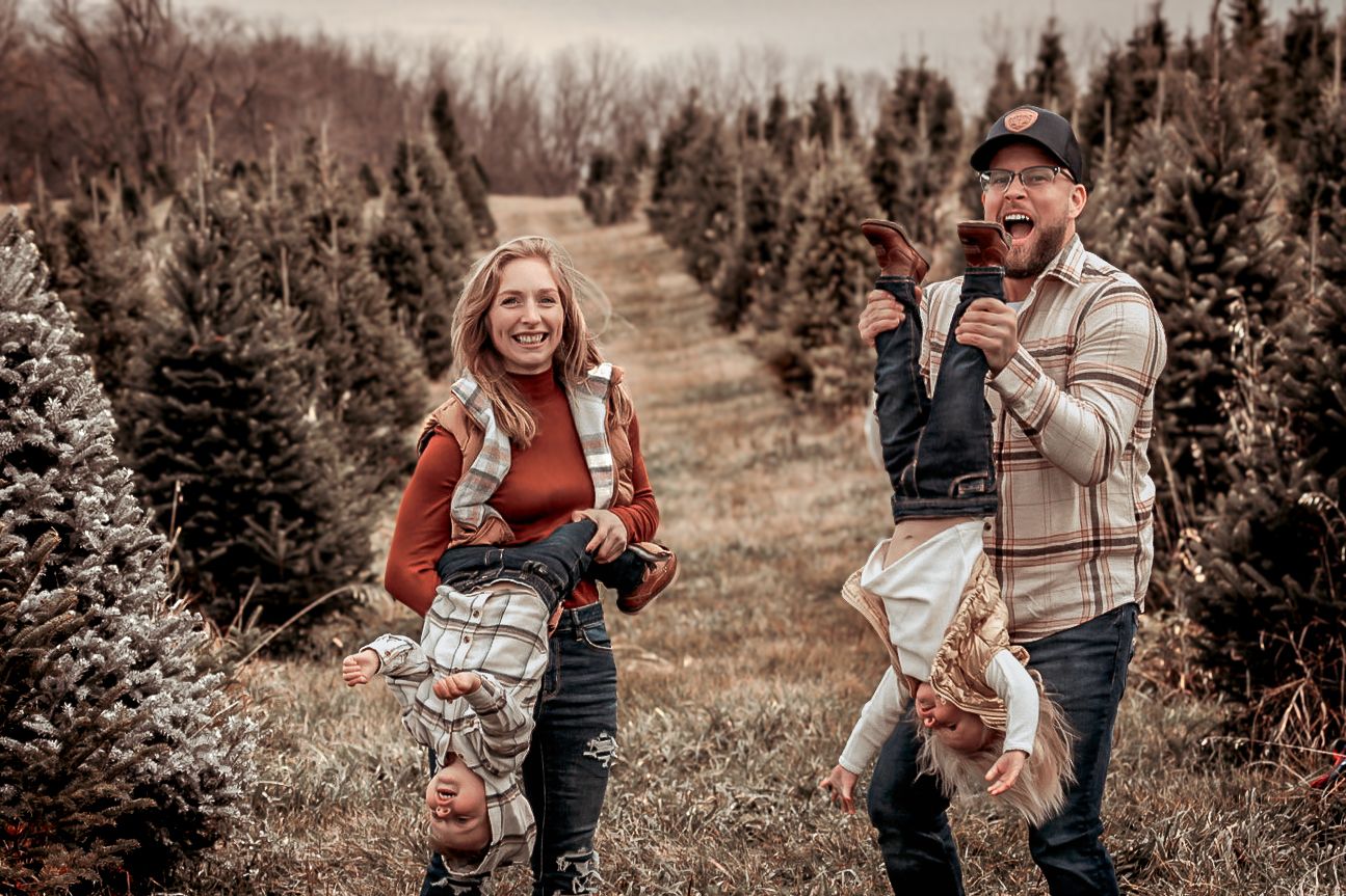 Candid family moments captured in soft light at a rustic outdoor tree farm setting.