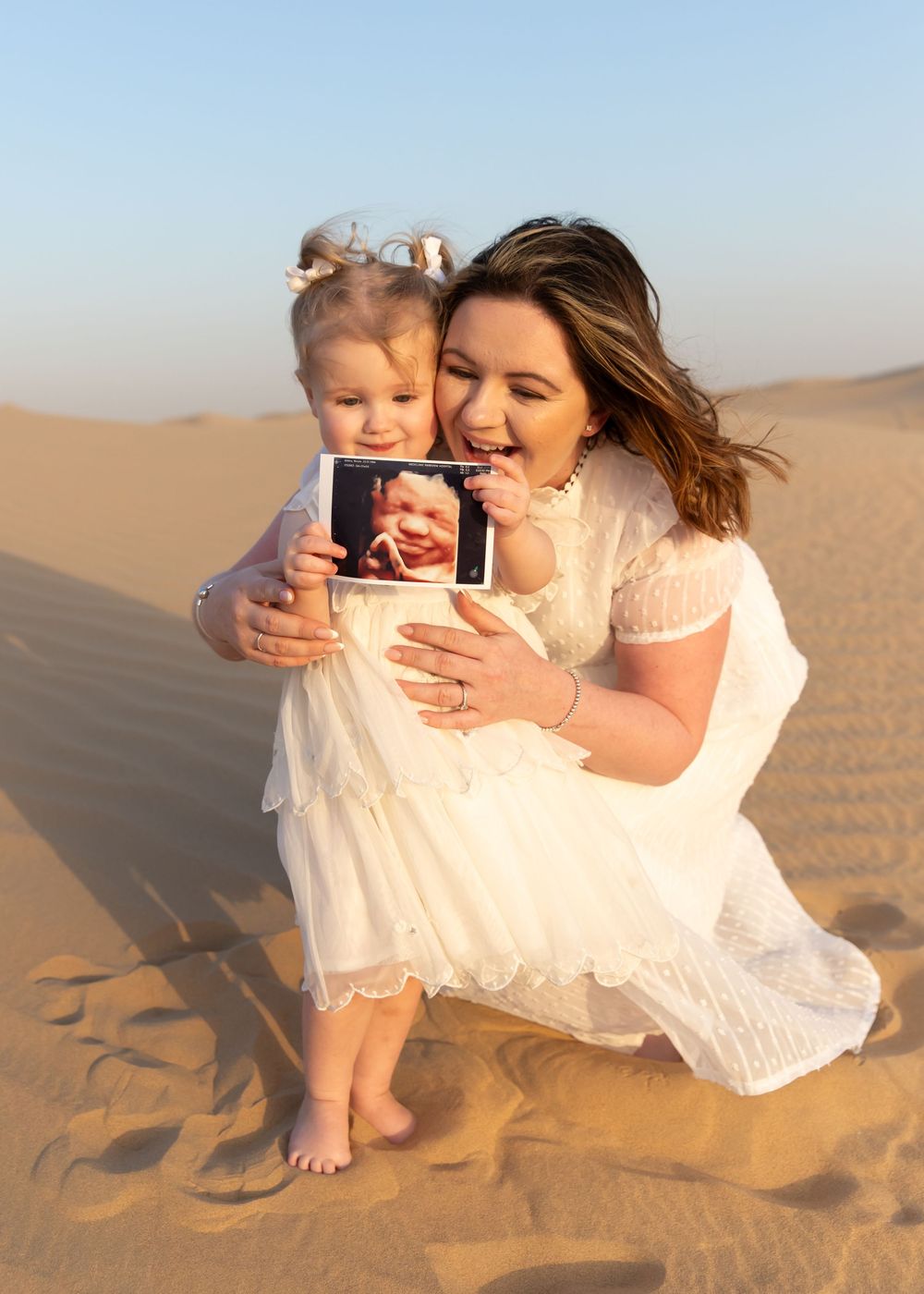 Pregnant mother and young toddler daughter holding new baby scan during desert family maternity photoshoot in Dubai