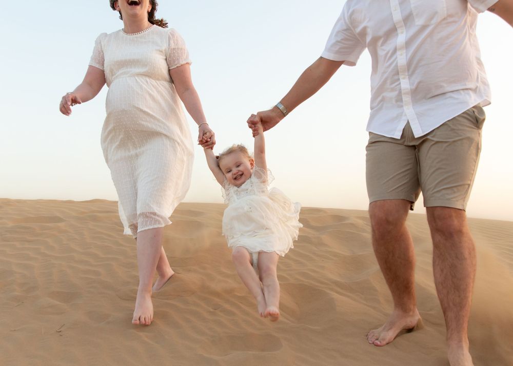 parents and young toddler girl running down a desert dune laughing dubai during an outdoor family photoshoot