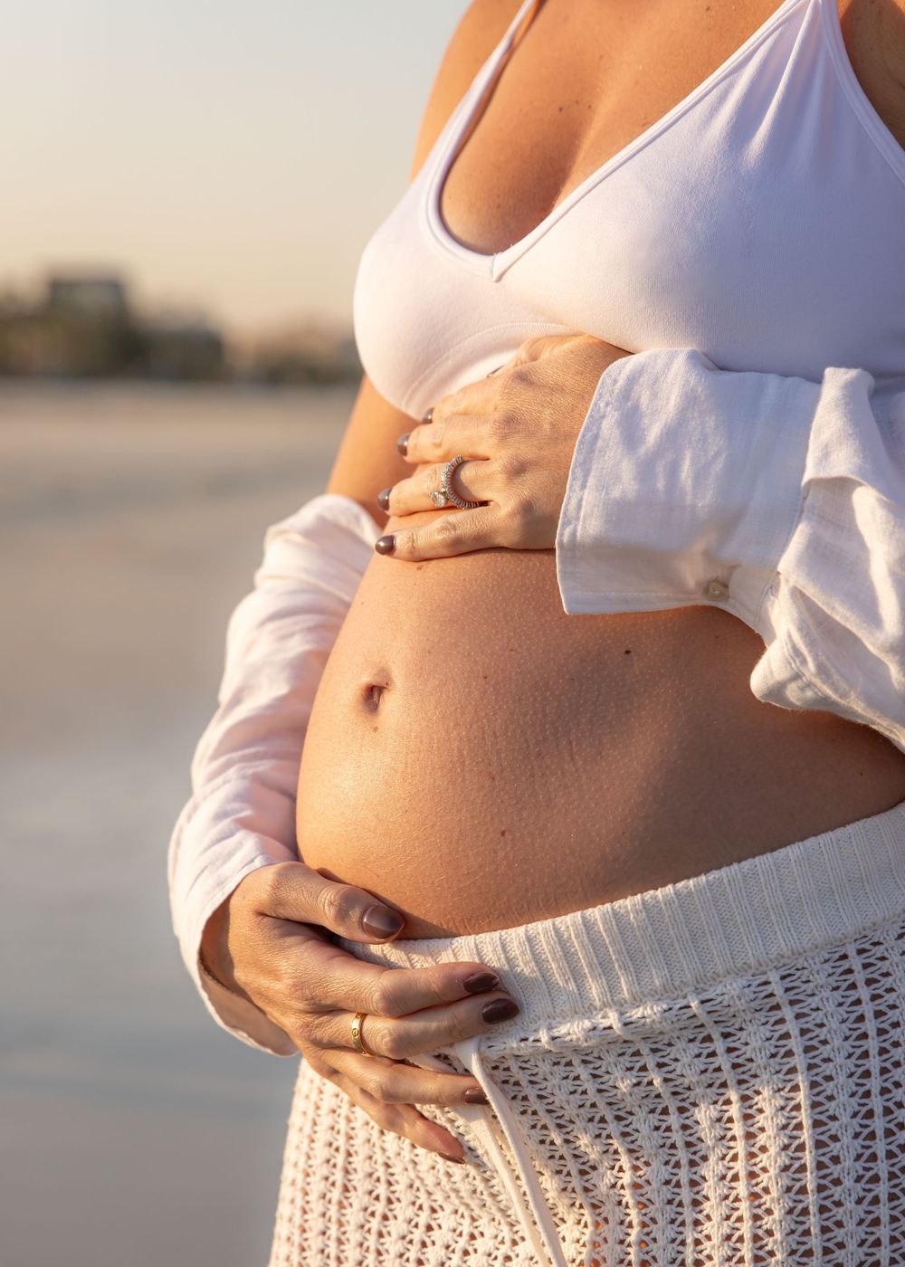close up of expecting mother's hands on her bare belly on the beach in Dubai during maternity family photography session