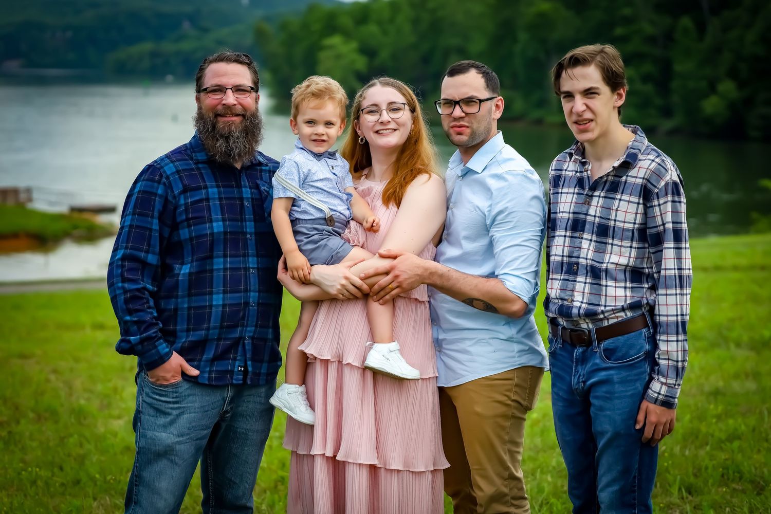 Casual family group portrait in plaid shirts against green landscape.