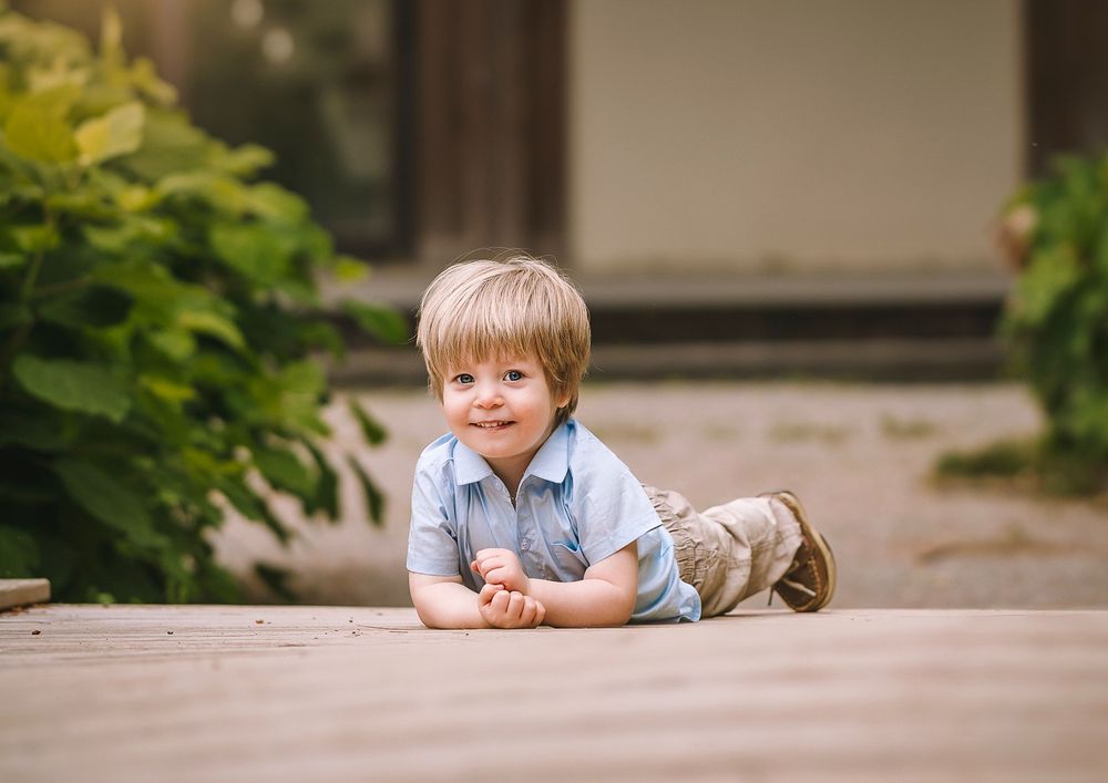 A child lies on their stomach on a concrete surface while looking at something on the ground.