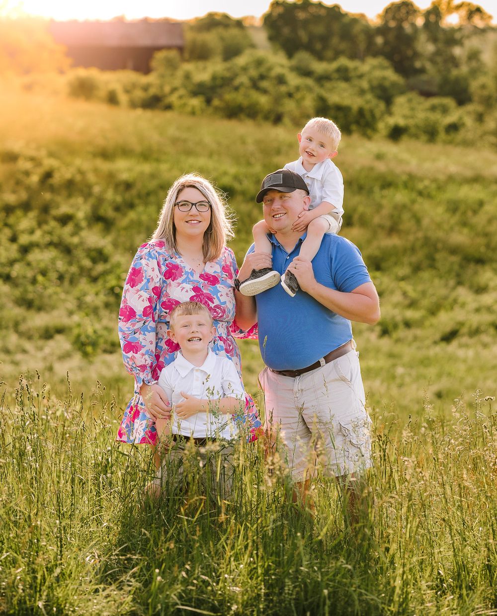 A family poses together in a sunlit meadow with tall grass during golden hour at sunset.