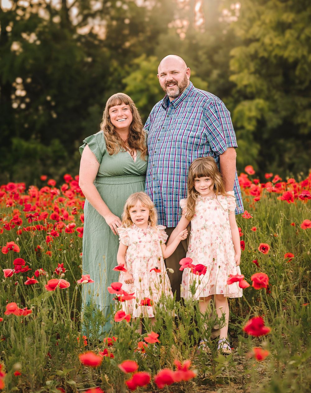 A family poses together in a vibrant field of red poppies during golden sunset hour.