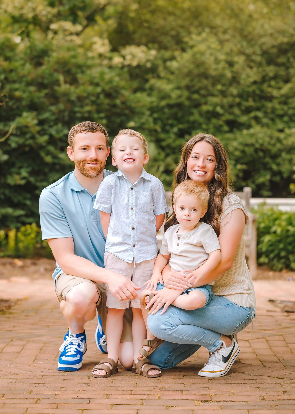 A family poses together on a brick patio with trees in the background during a golden sunset.
