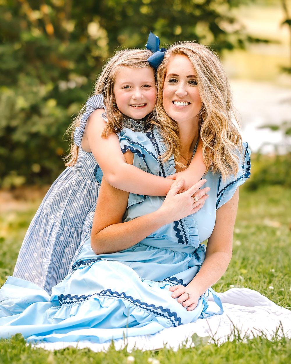 A touching outdoor portrait showing two people wearing matching light blue dresses sitting together on a blanket in nature.