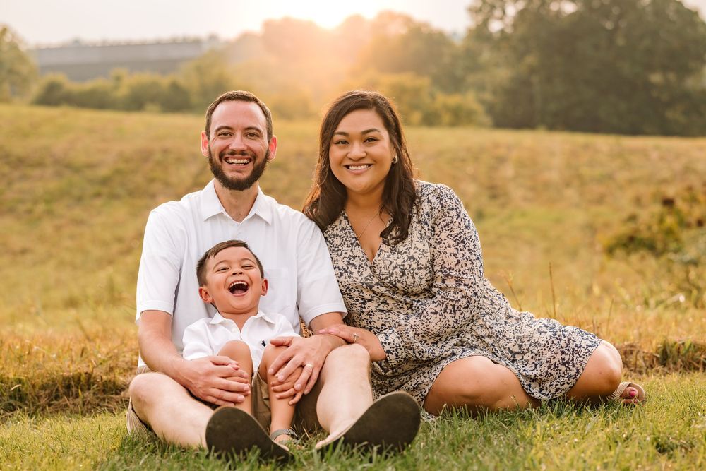Family enjoying sunset together on grassy hillside in golden light.