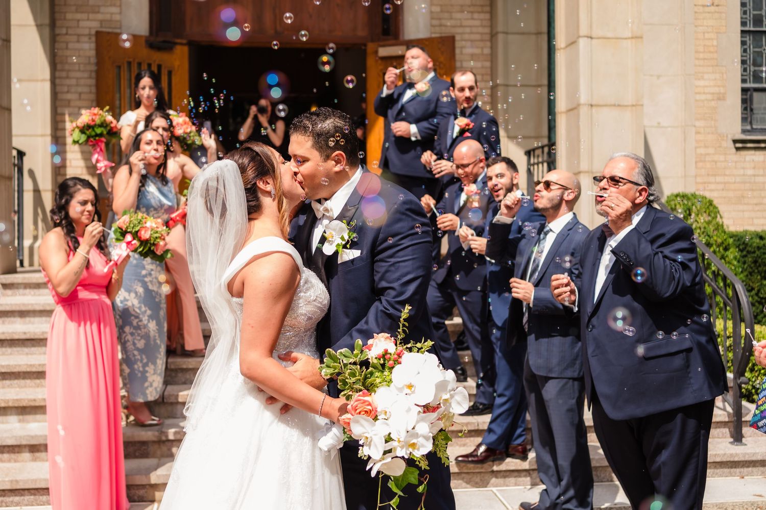 Wedding party celebrates on church steps while guests capture the moment.