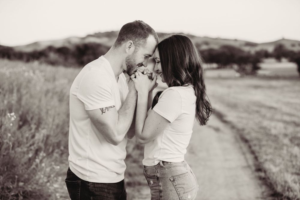 A romantic black and white photo of a couple sharing an intimate moment in a rural field setting.