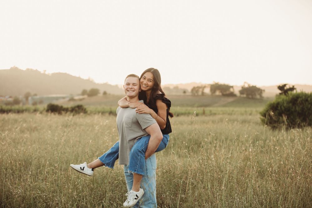 Two friends enjoying a playful piggyback ride in a golden meadow at sunset with mountains in the distance.