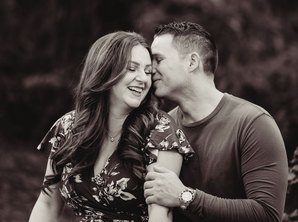 A romantic couple embraces while sharing a joyful moment with spring flowers in a black and white portrait.
