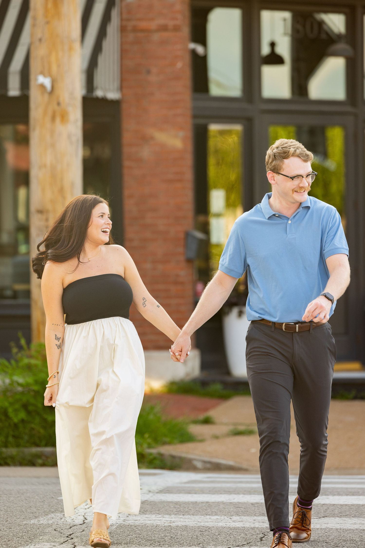 A young couple hold hands and walk together on a city street.