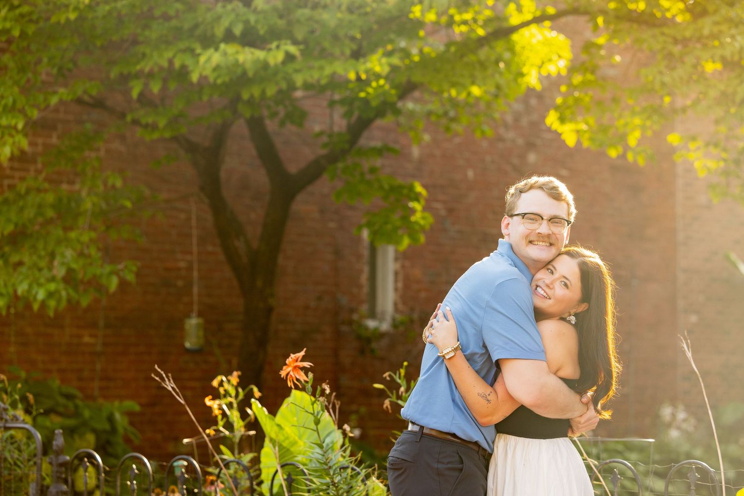 A young couple embrace and smile while standing in a park.