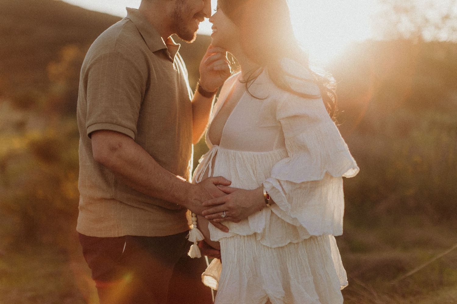 A couple shares an intimate moment in soft golden sunlight outdoors. San Diego Maternity Photography.