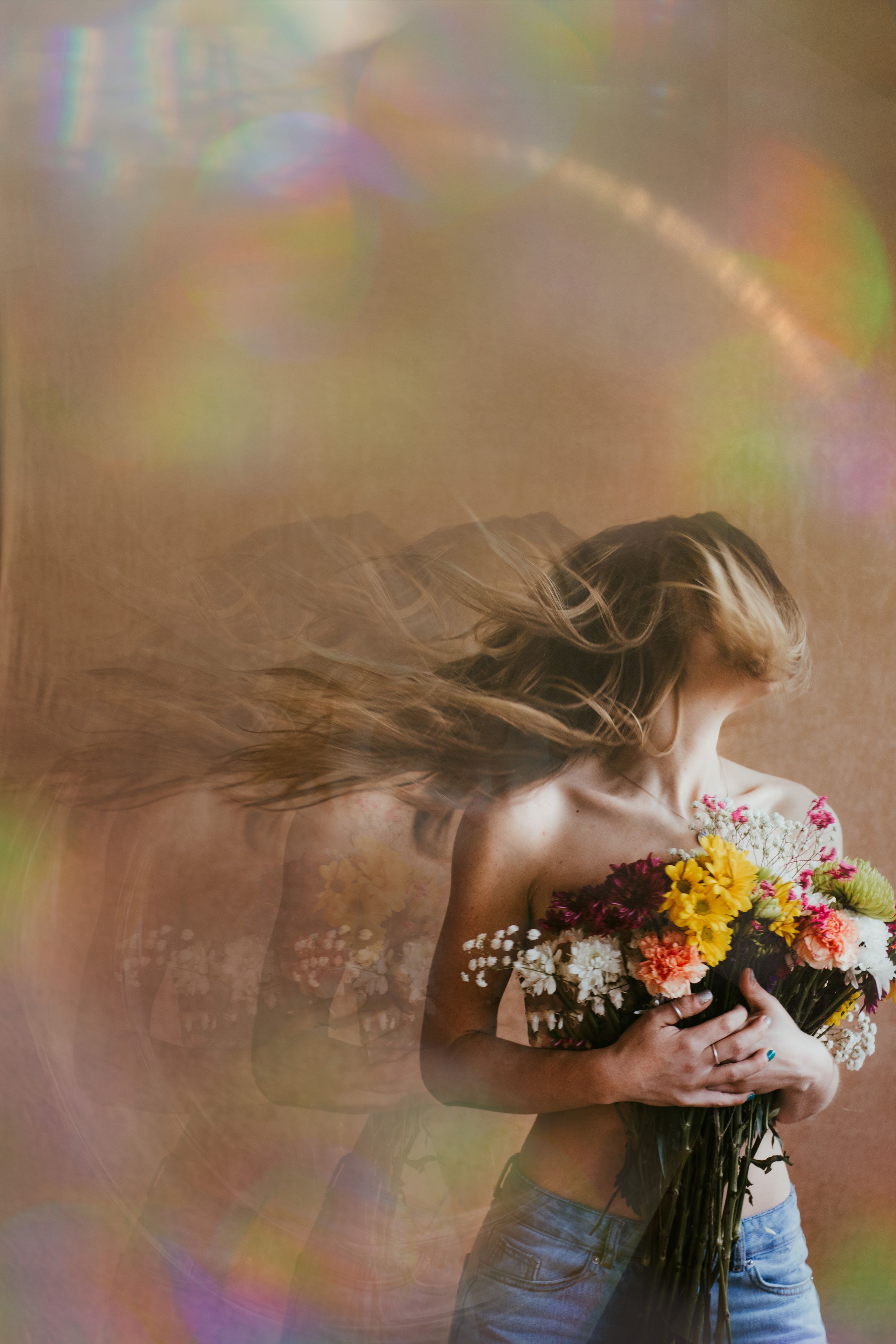 Artistic portrait of someone holding a vibrant bouquet of flowers with rainbow light effects.