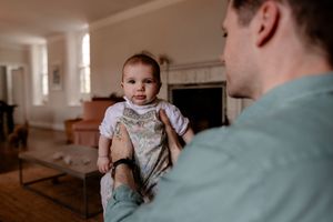 A father holds his baby in a bright living room with a fireplace, sharing a tender moment together.