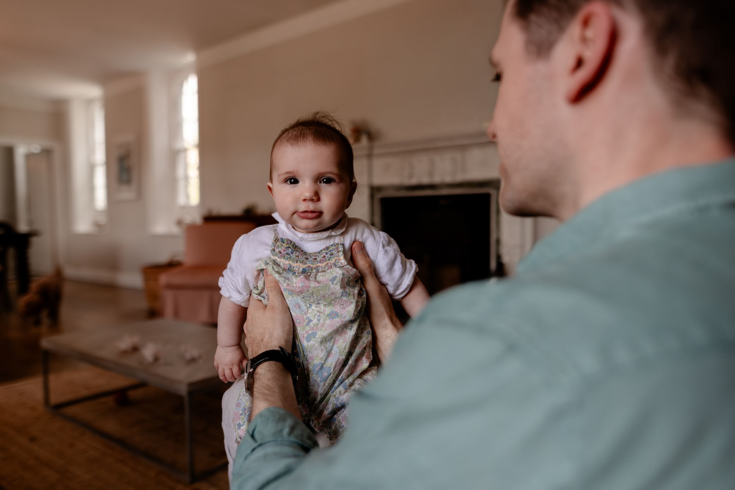 A father holds his baby in a bright living room with a fireplace, sharing a tender moment together.