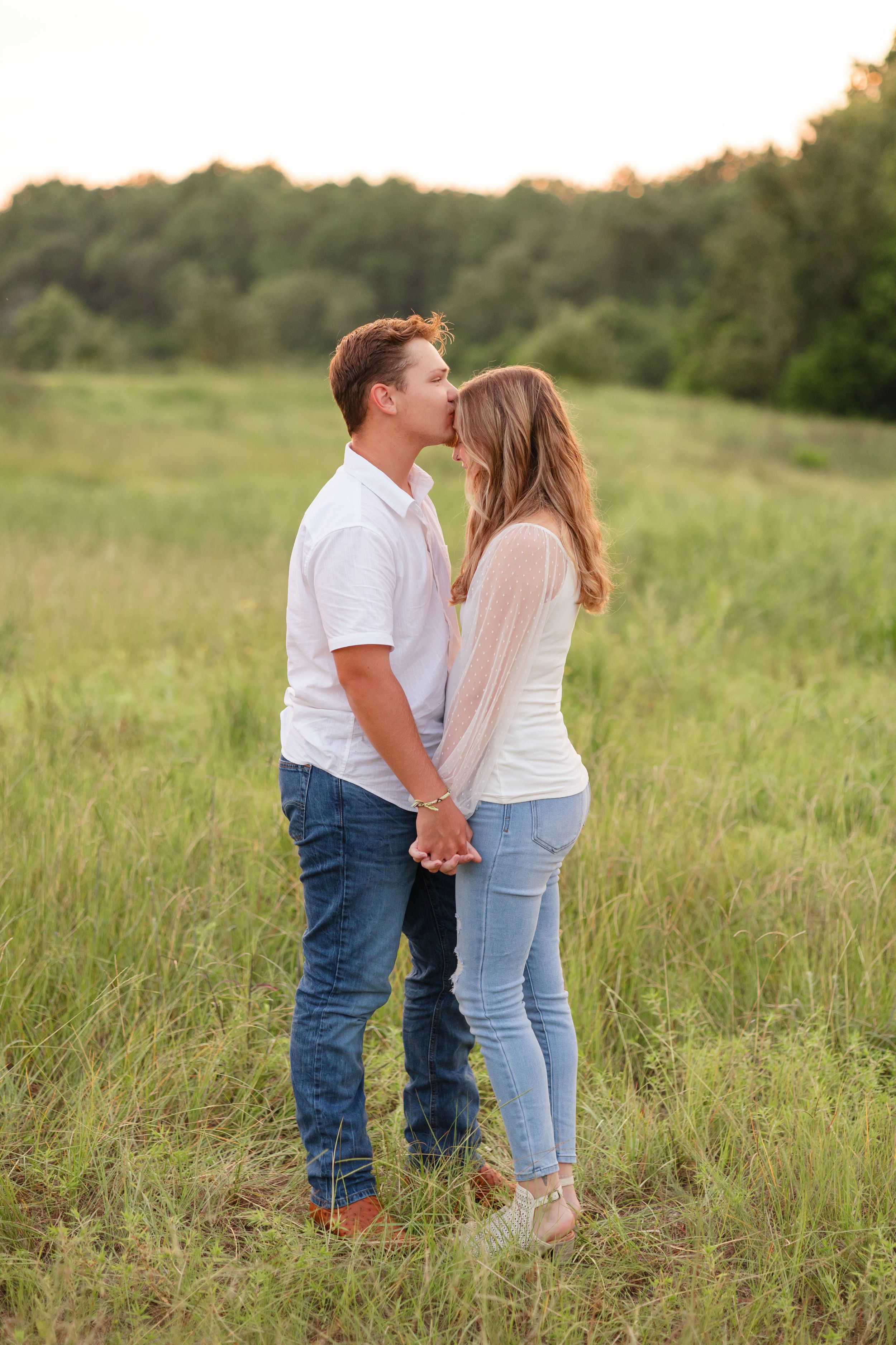 A romantic couple embraces in a sunlit meadow during golden hour.