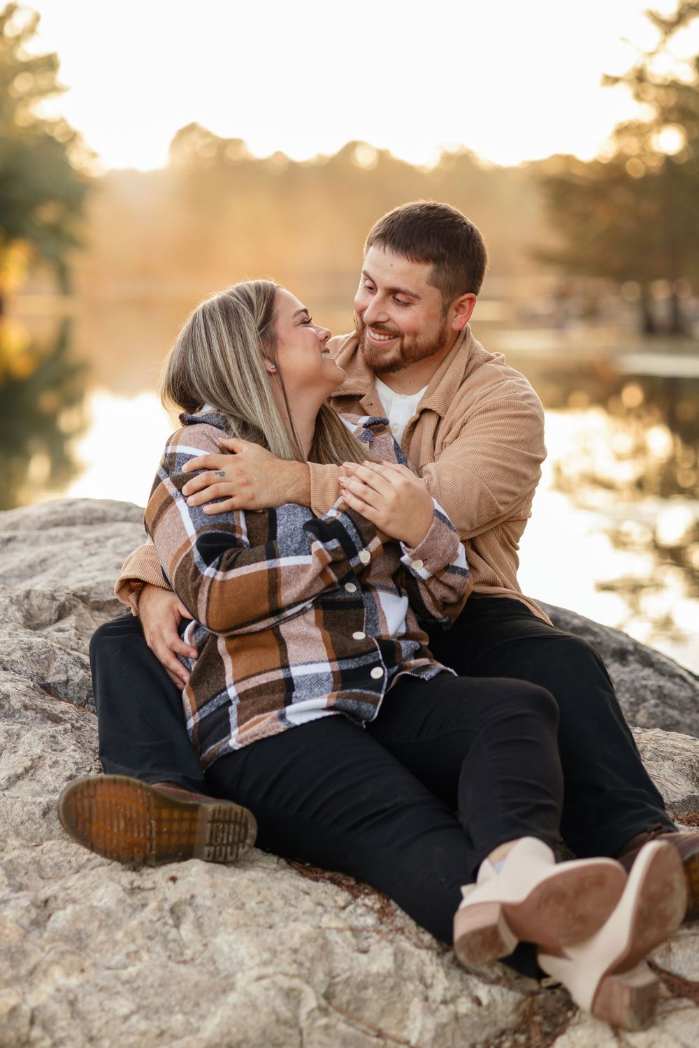 Intimate couple sharing tender moment while sitting on rock by lake at sunset.