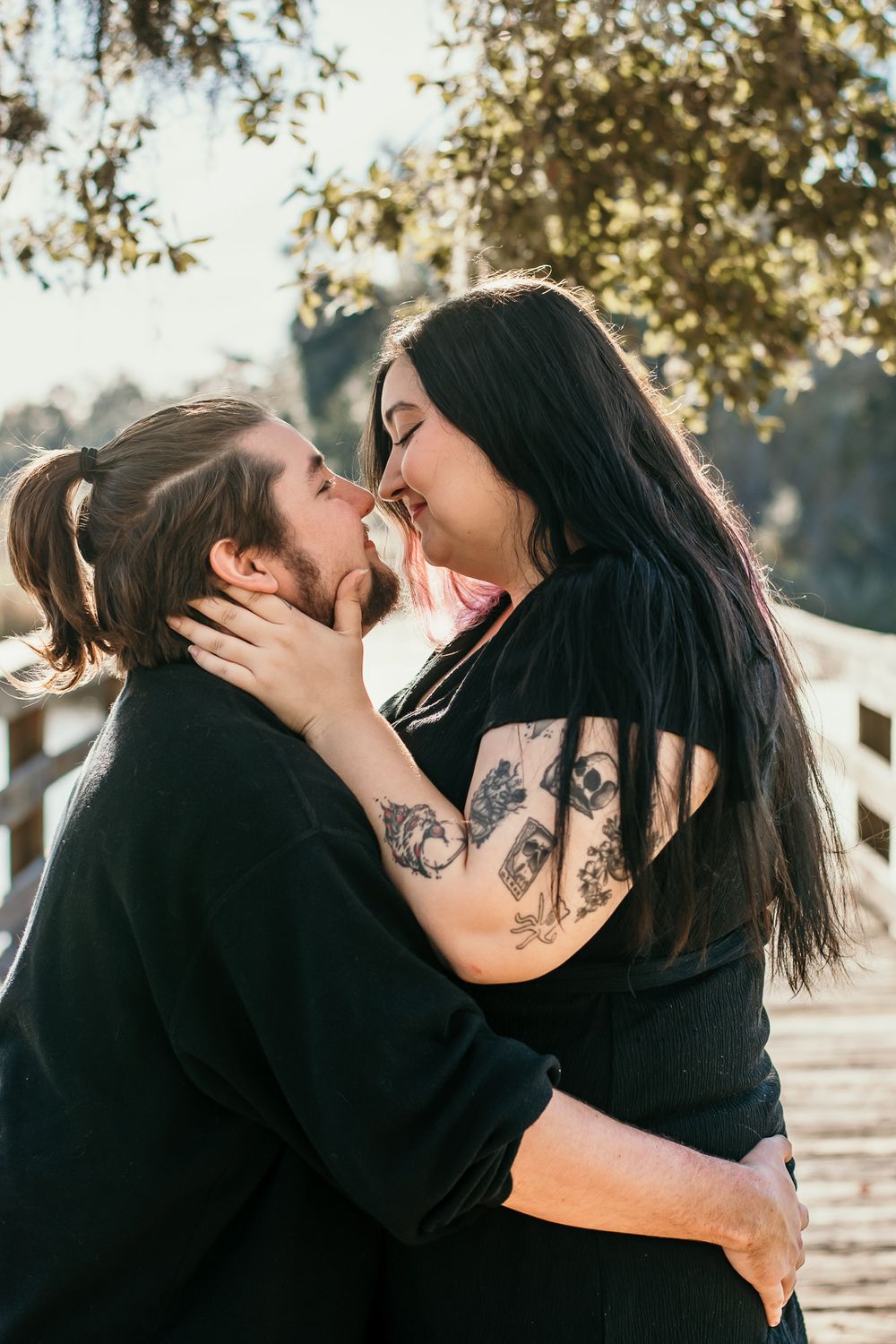 Intimate romantic moment between couple in black clothing on a sunlit bridge.