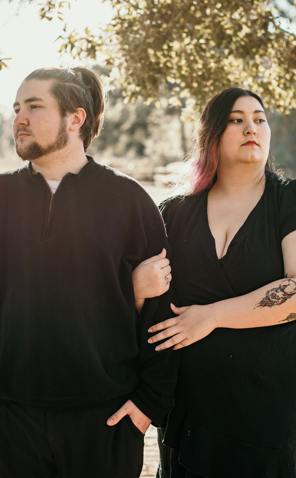 Stylish couple in black clothing pose dramatically on wooden walkway.