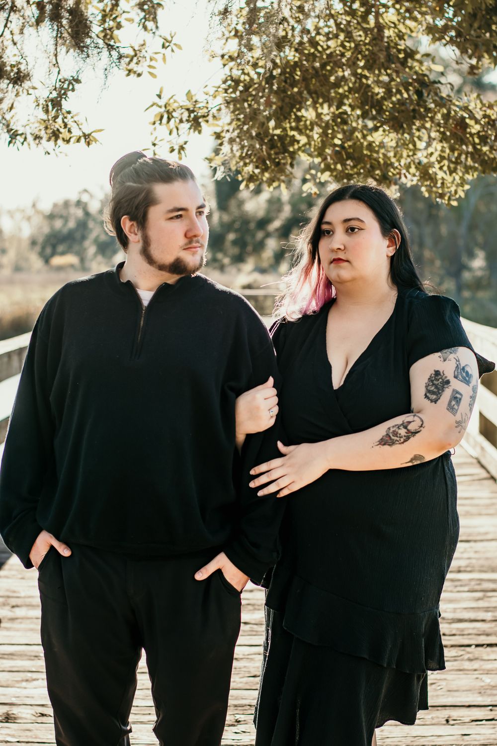 Couple in matching black outfits standing together on wooden boardwalk.
