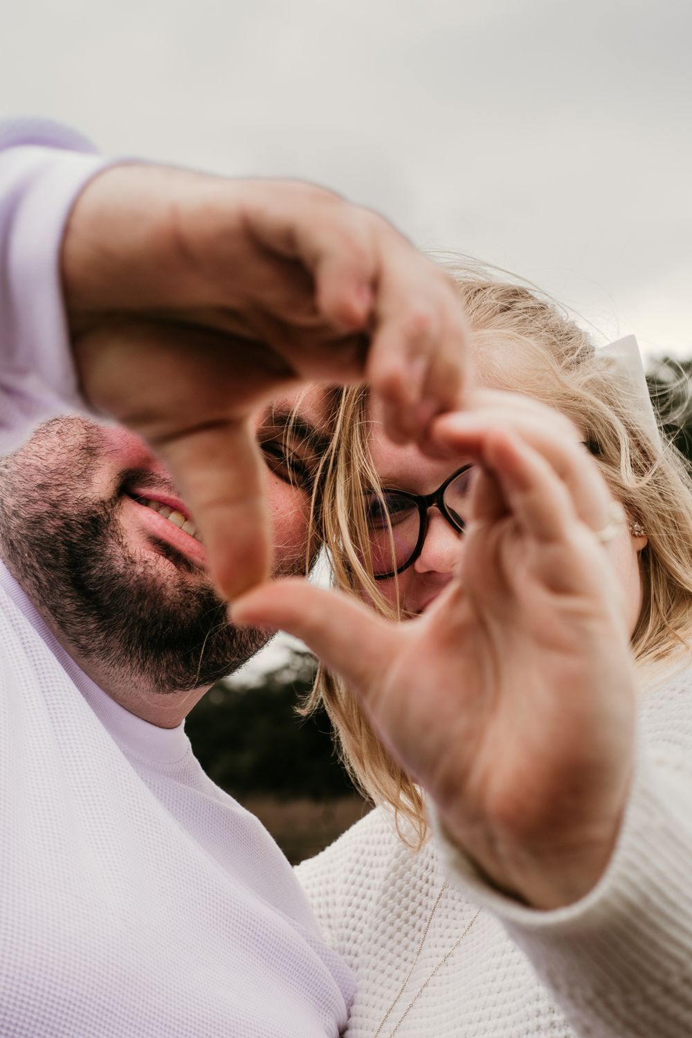 A couple forms a heart shape with their hands while looking up at the camera from below in a romantic pose.