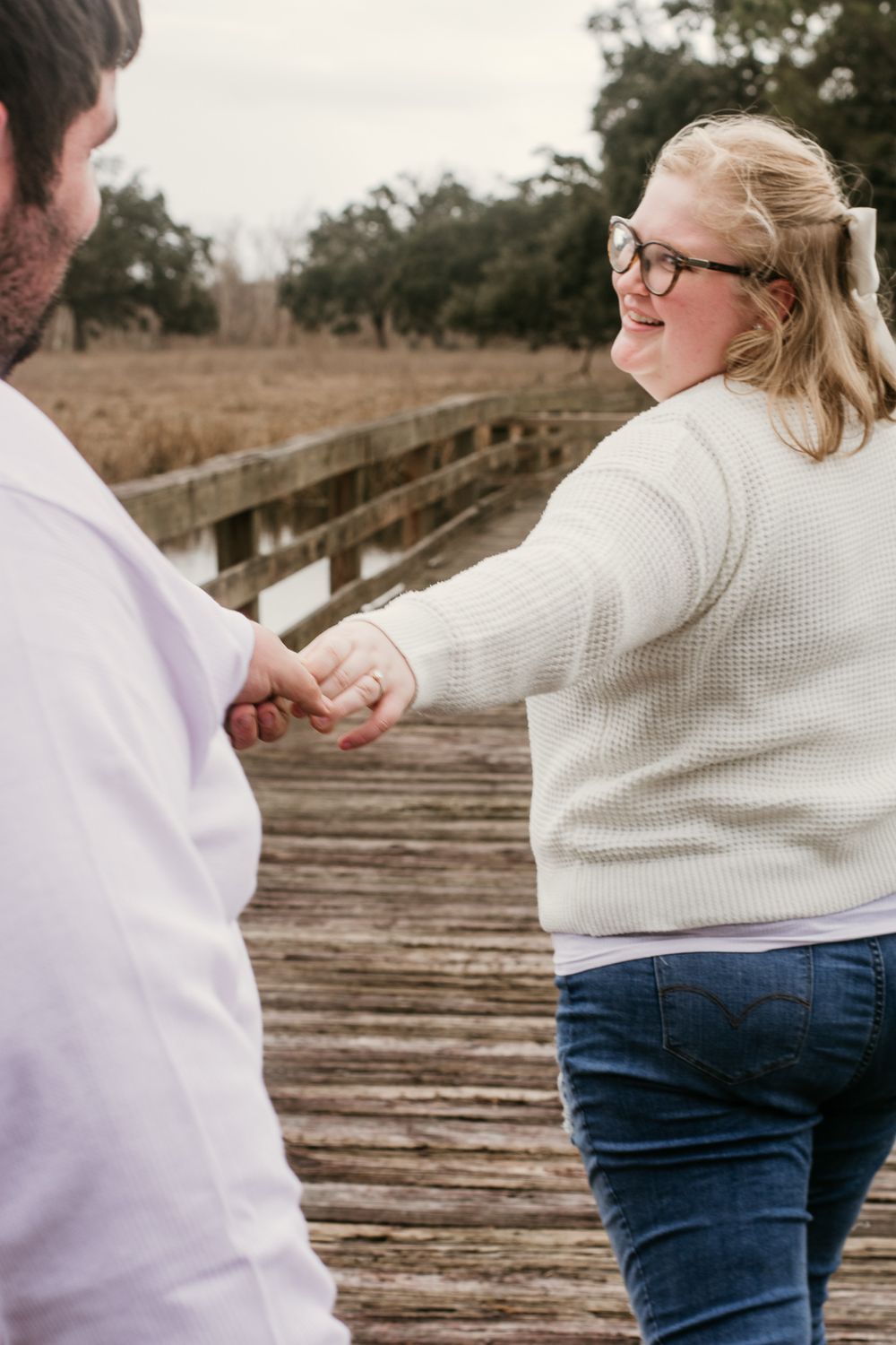 A couple holding hands while walking on a wooden boardwalk surrounded by autumn foliage.
