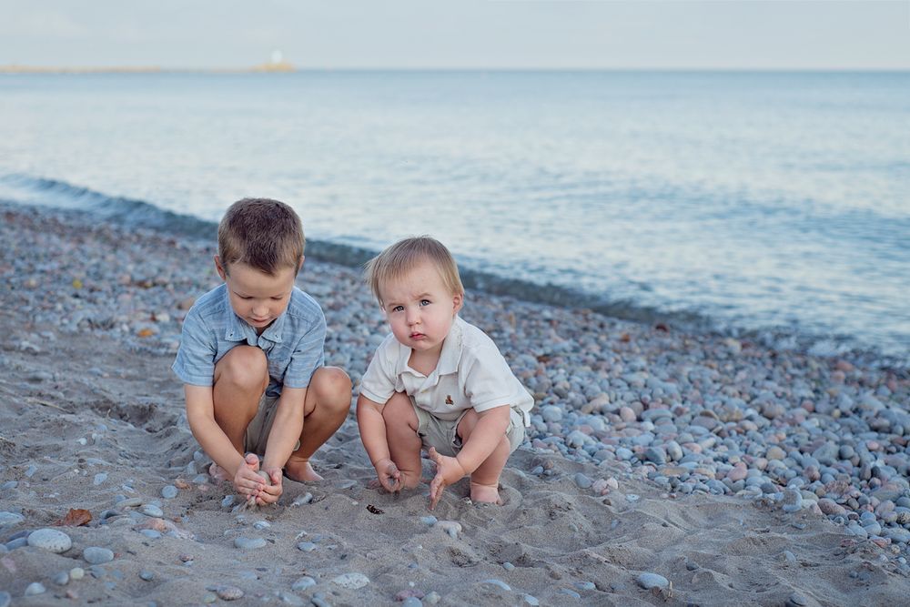 2 little boys crouch in the sand at the beach