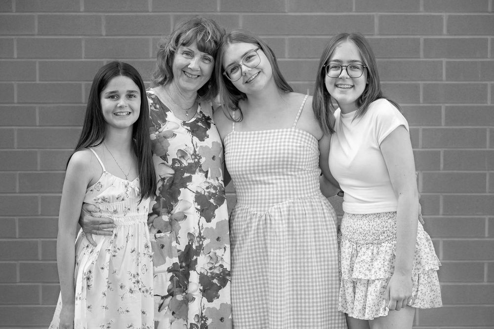 Black and white close up portrait of Grandmother with 3 teen age granddaughters hugging and smiling  together standing against a brick wall*