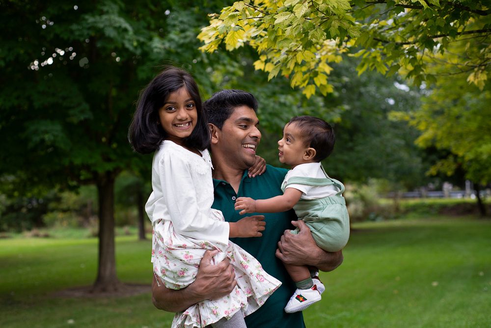 proud father holds his two young children smiling and naturally, outdoors at Bowmanville Vally Conservation Area*