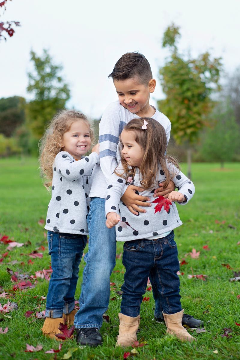 Lifestyle outdoor photography, three siblings playing in fall leaves in Bowmanville Vally Conservation Area, Ontario*
