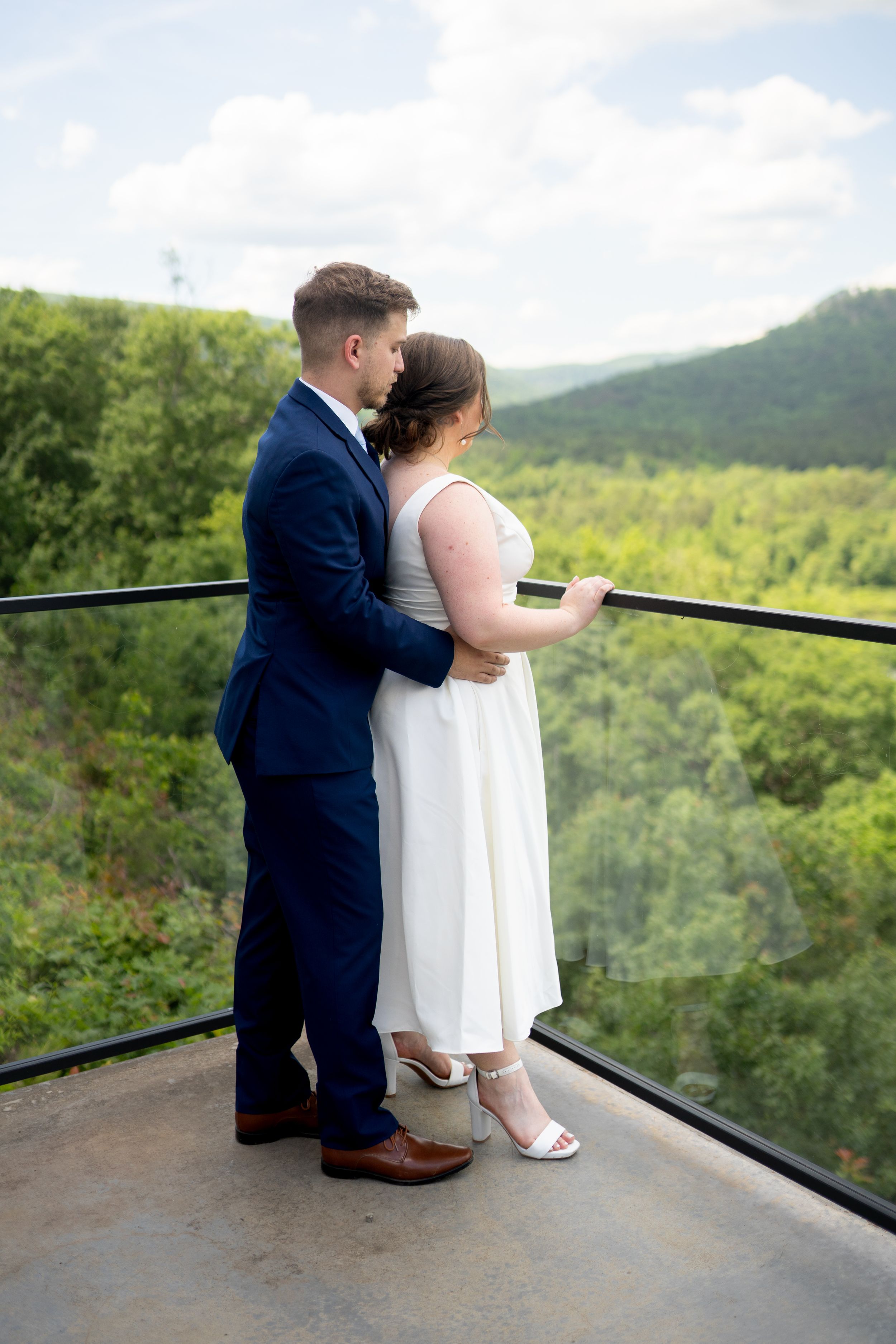 Wedding couple shares quiet moment together on scenic mountain overlook deck.