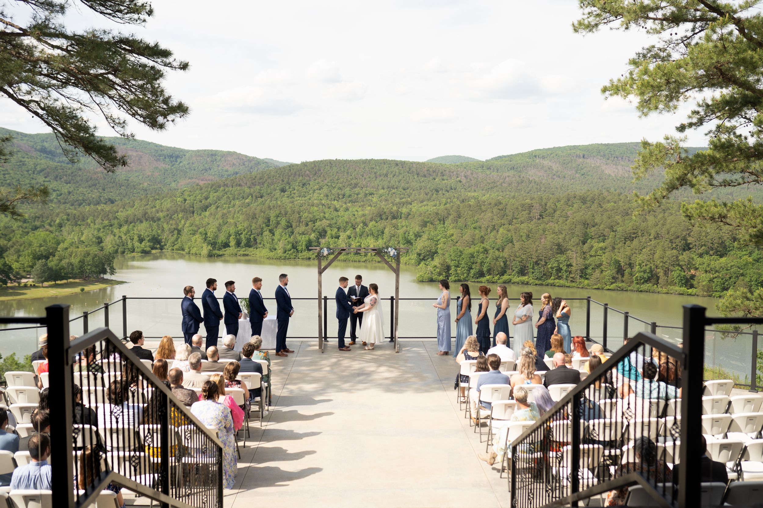 Panoramic view of wedding ceremony setup on mountain overlook with guests arriving.