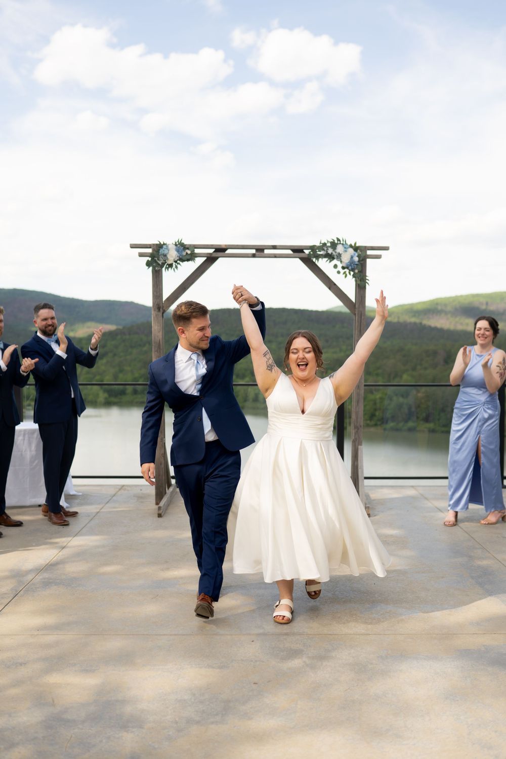 Wedding couple celebrates and dances together at outdoor mountain venue with guests.