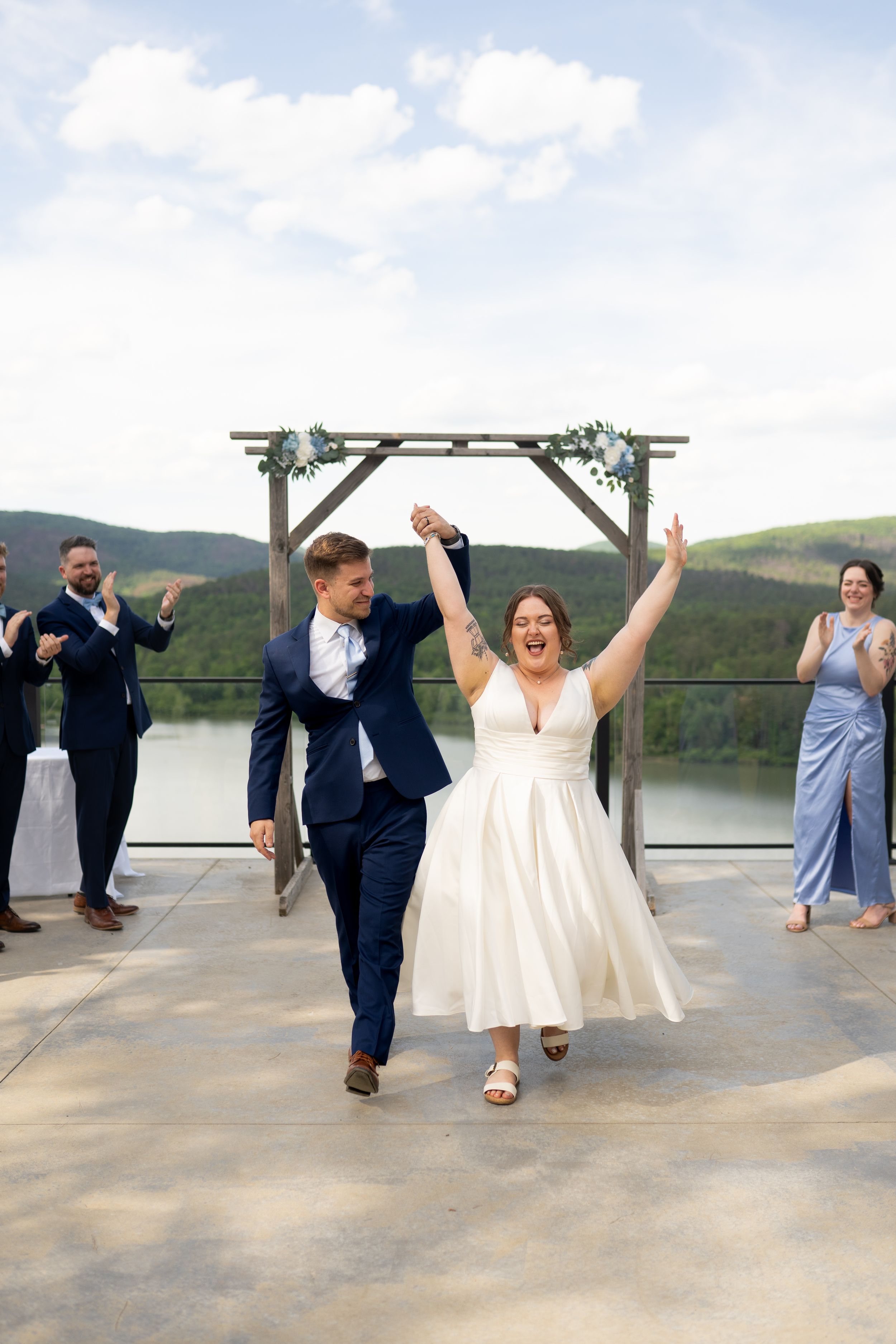 Wedding couple celebrates and dances together at outdoor mountain venue with guests.