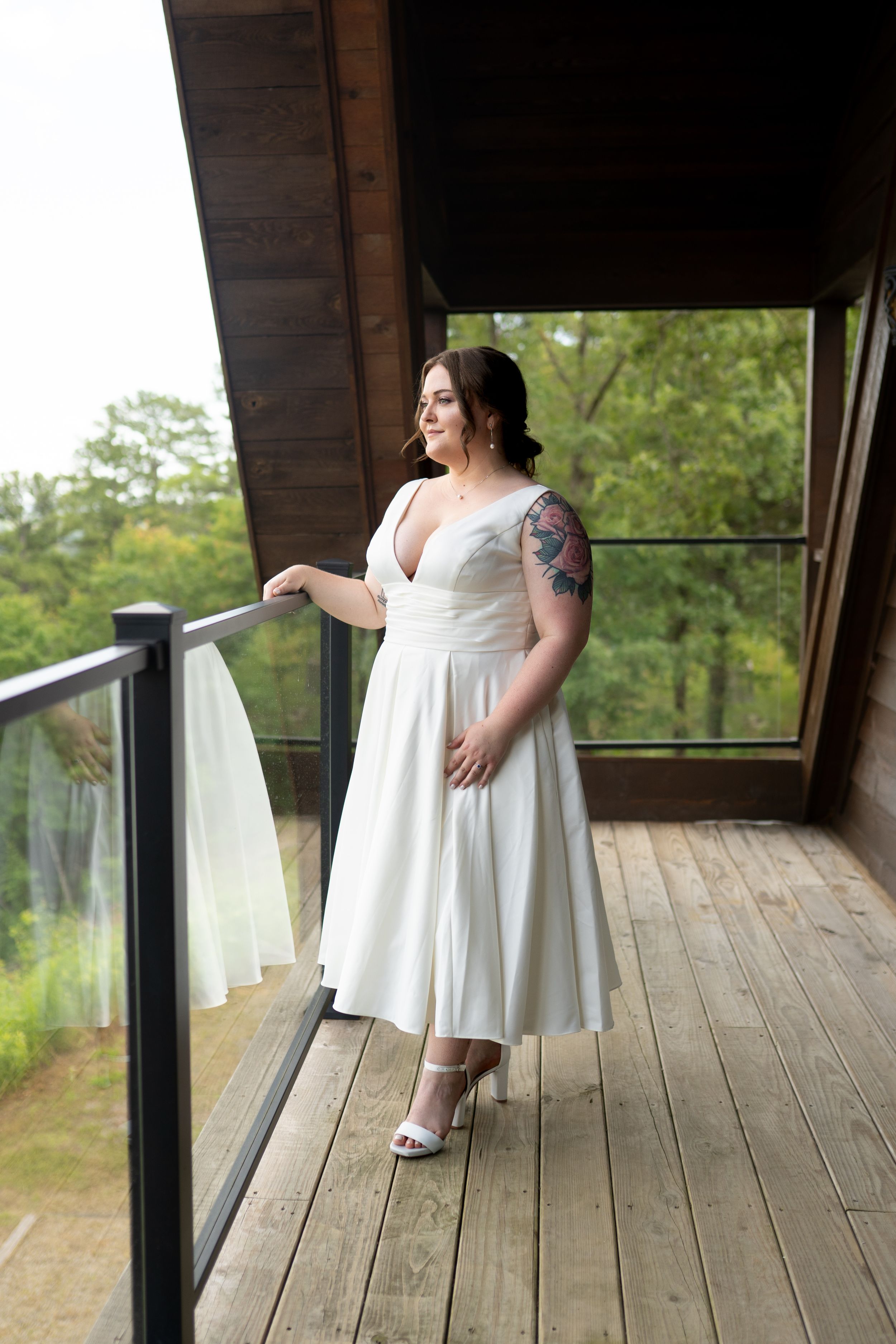 Bride in flowing white dress poses on rustic wooden deck with scenic view.