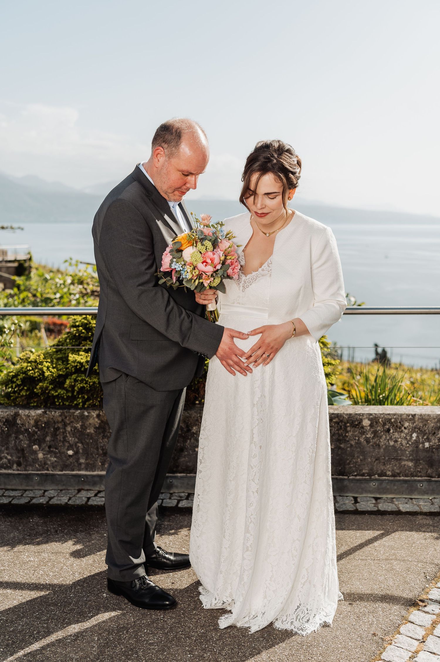 A couple in wedding attire dances together on a stone terrace with ocean views.