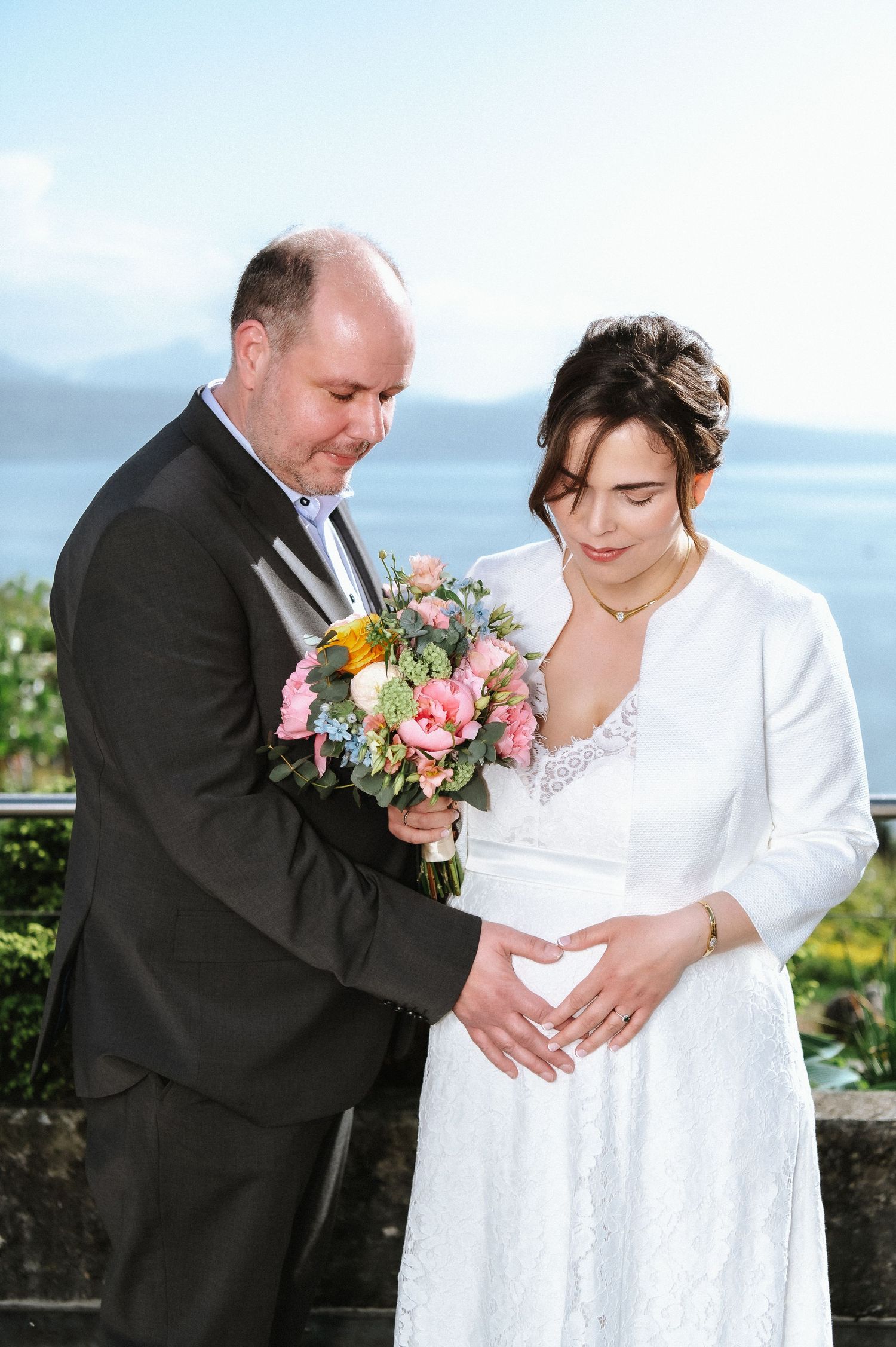 Newlyweds share an intimate moment while holding a pink and peach floral bouquet.