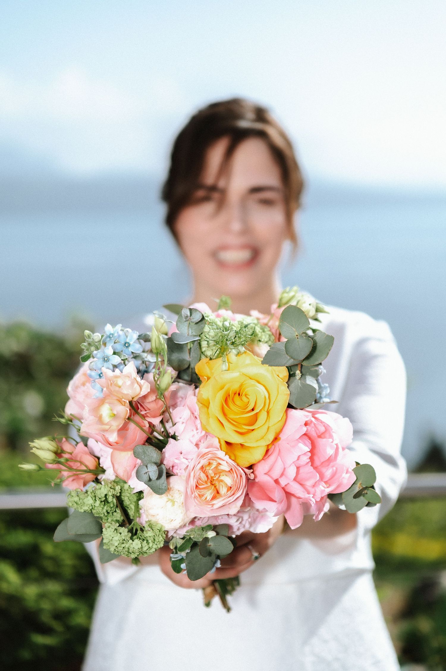 Beautiful wedding bouquet featuring yellow roses, pink flowers, and eucalyptus against an ocean backdrop.