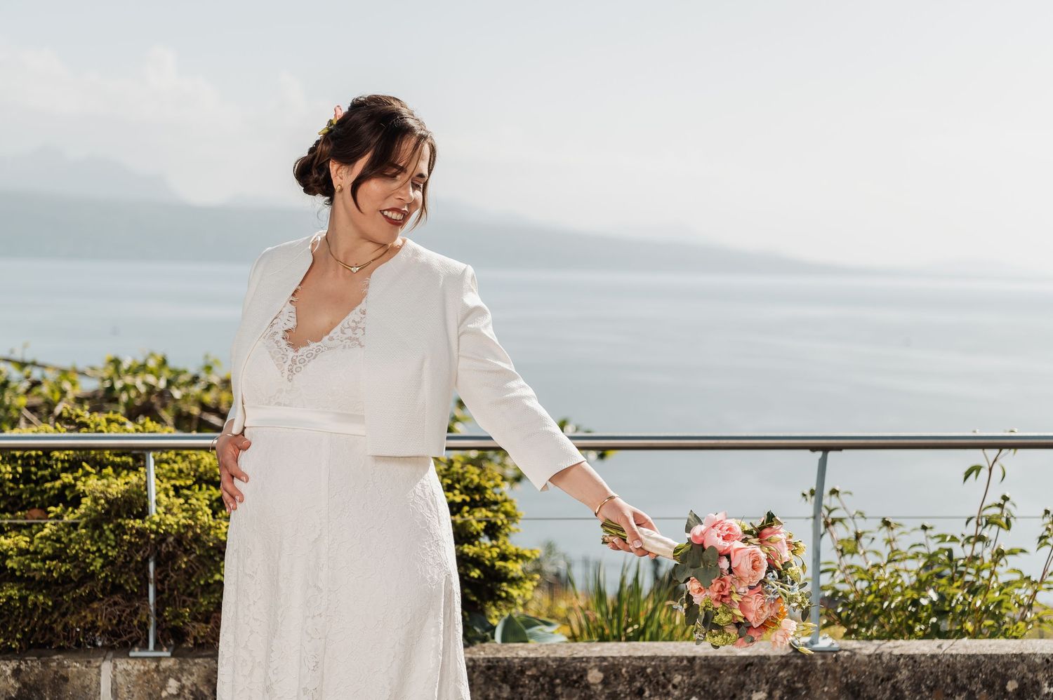 A bride in a white dress poses gracefully on a stone terrace overlooking the sea.