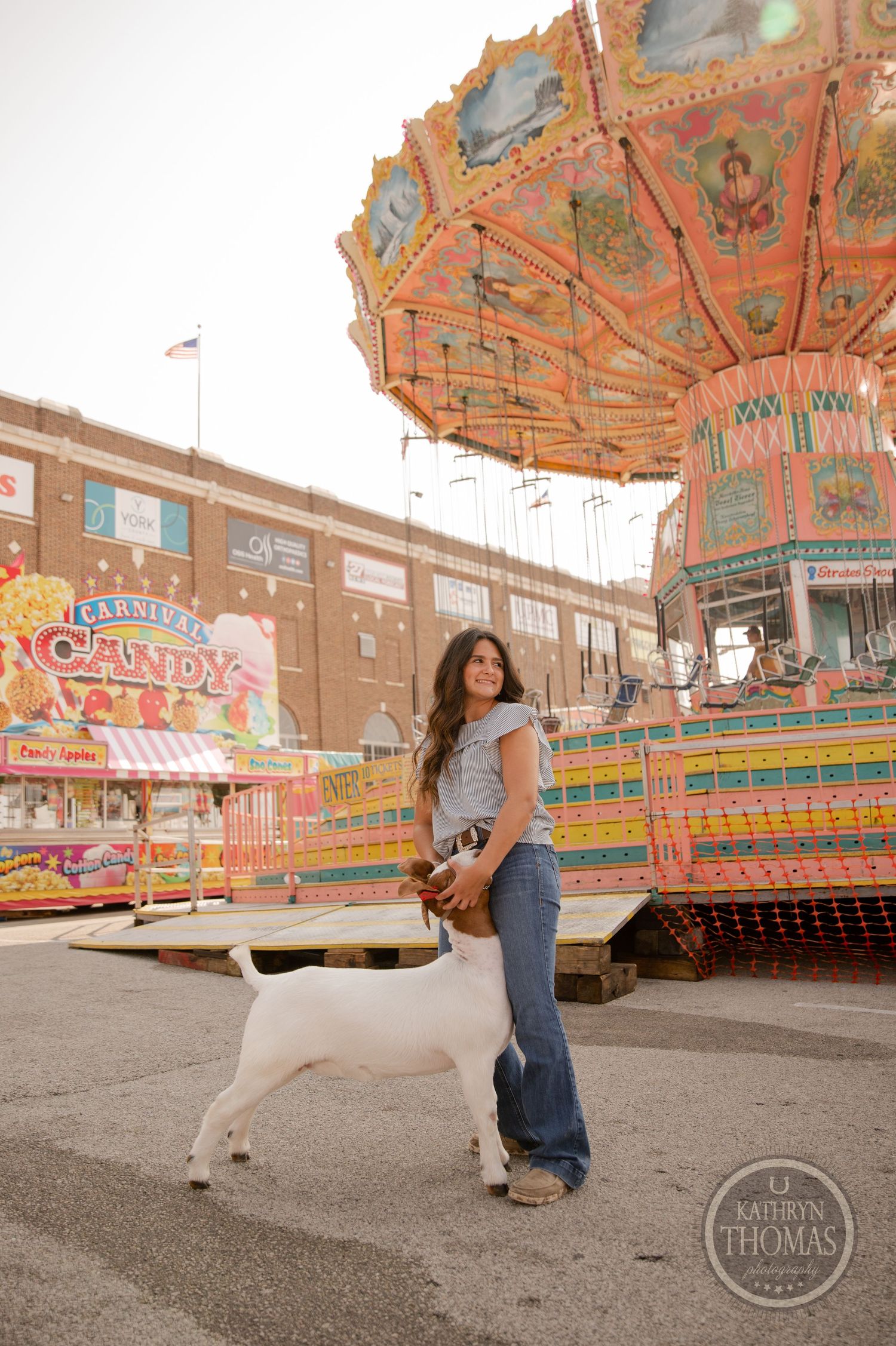 A white dog and their companion pose in front of a colorful carnival carousel.
