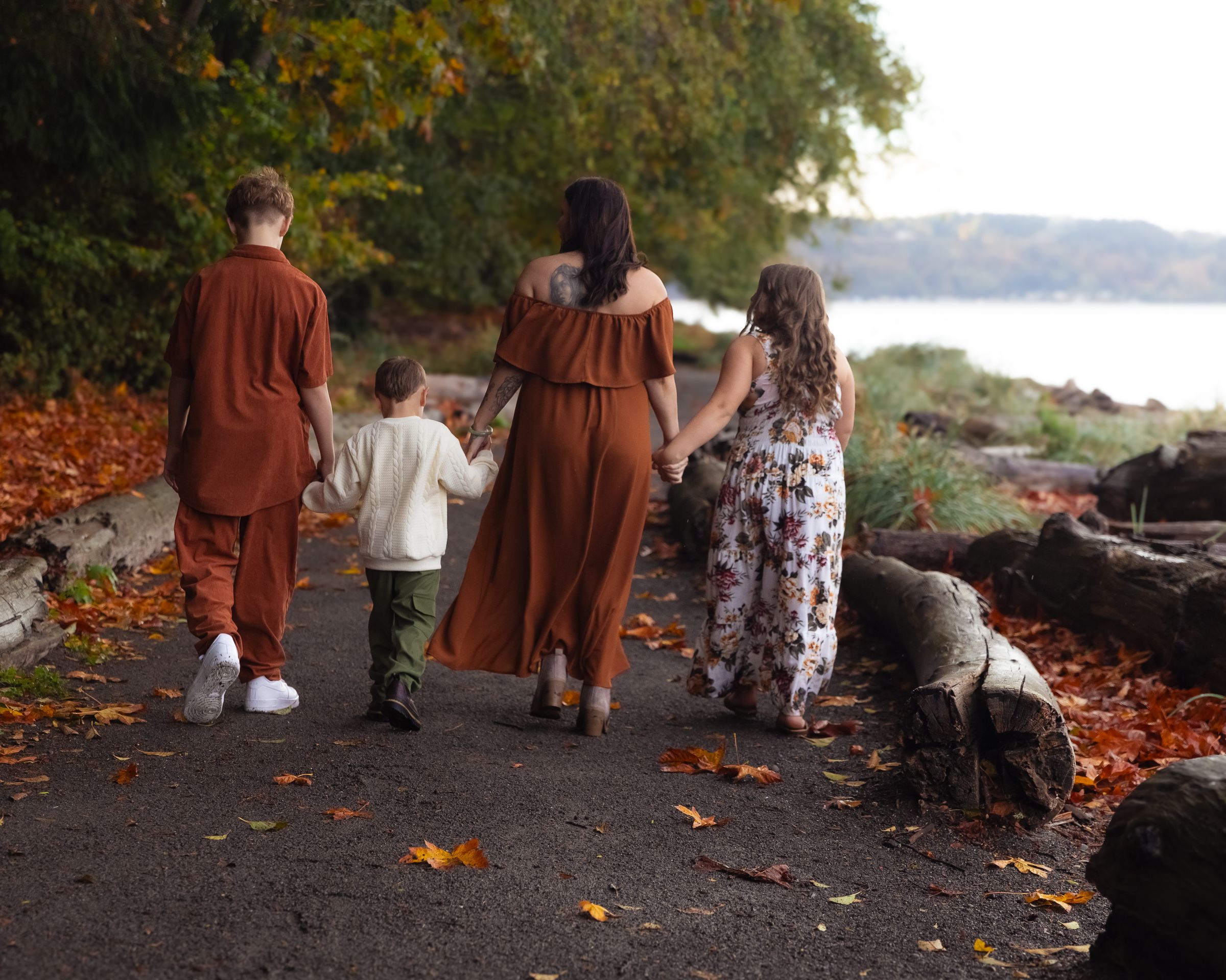 A family surrounded by orange fall foliage walk along a path at Owen Beach during a fall family session in Tacoma, Washington.