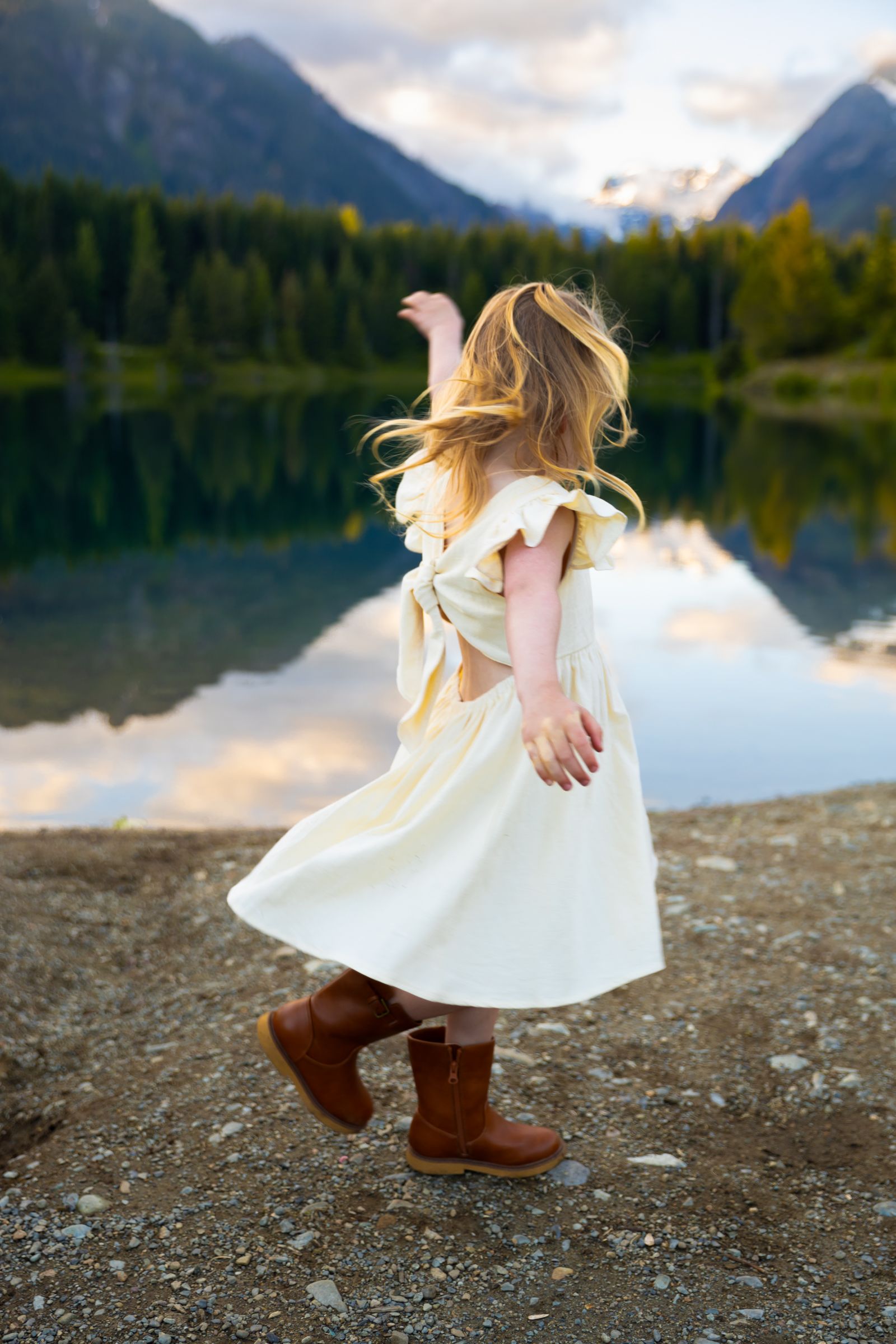 A girl twirls wildly in front of lake and mountain scene in a moment captured by Washington family photographer Jess Bickel.