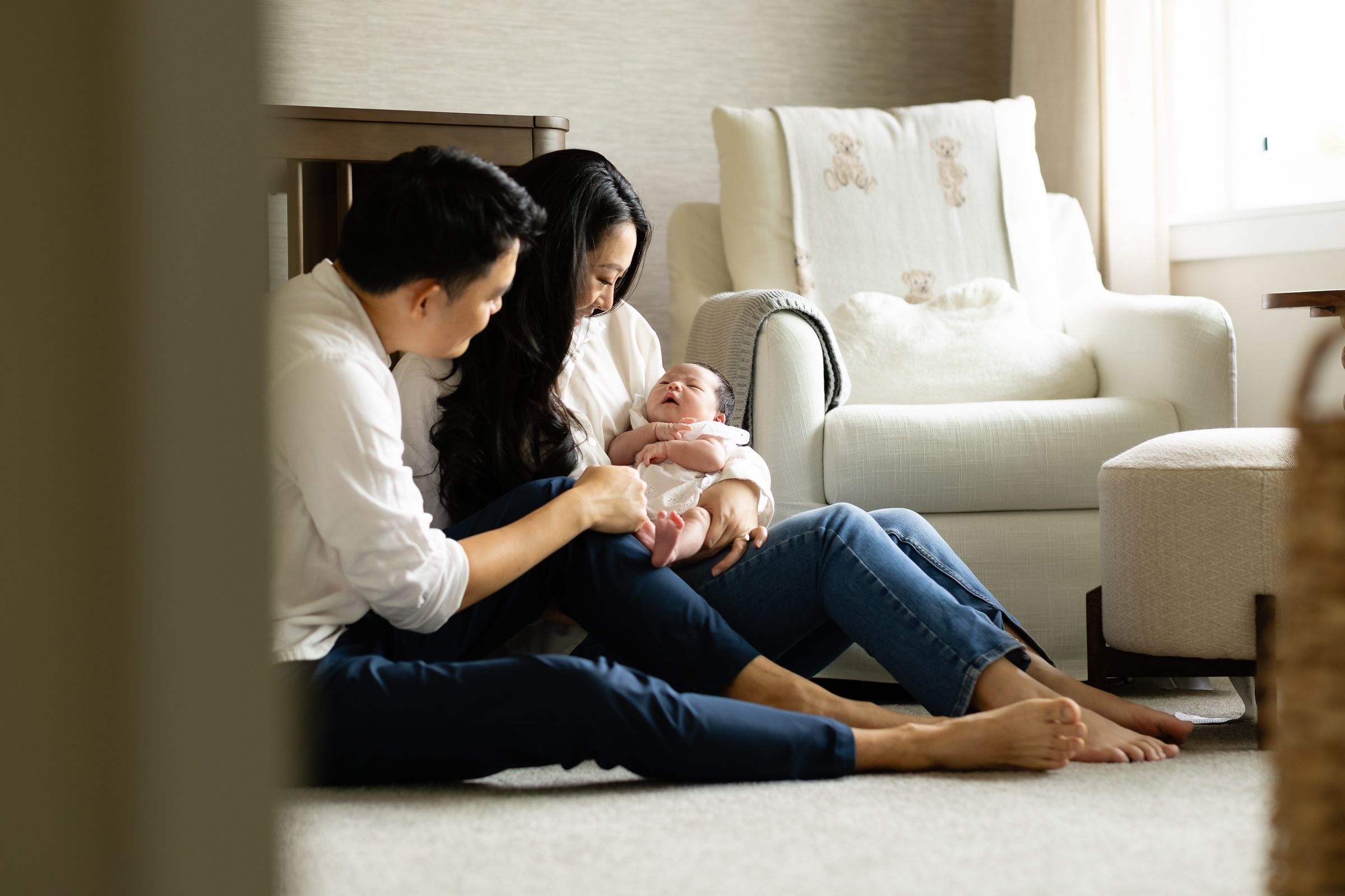 New mom and dad sit on their nursery floor holding their newborn baby during their lifestyle newborn session in Bonney Lake, Washington.