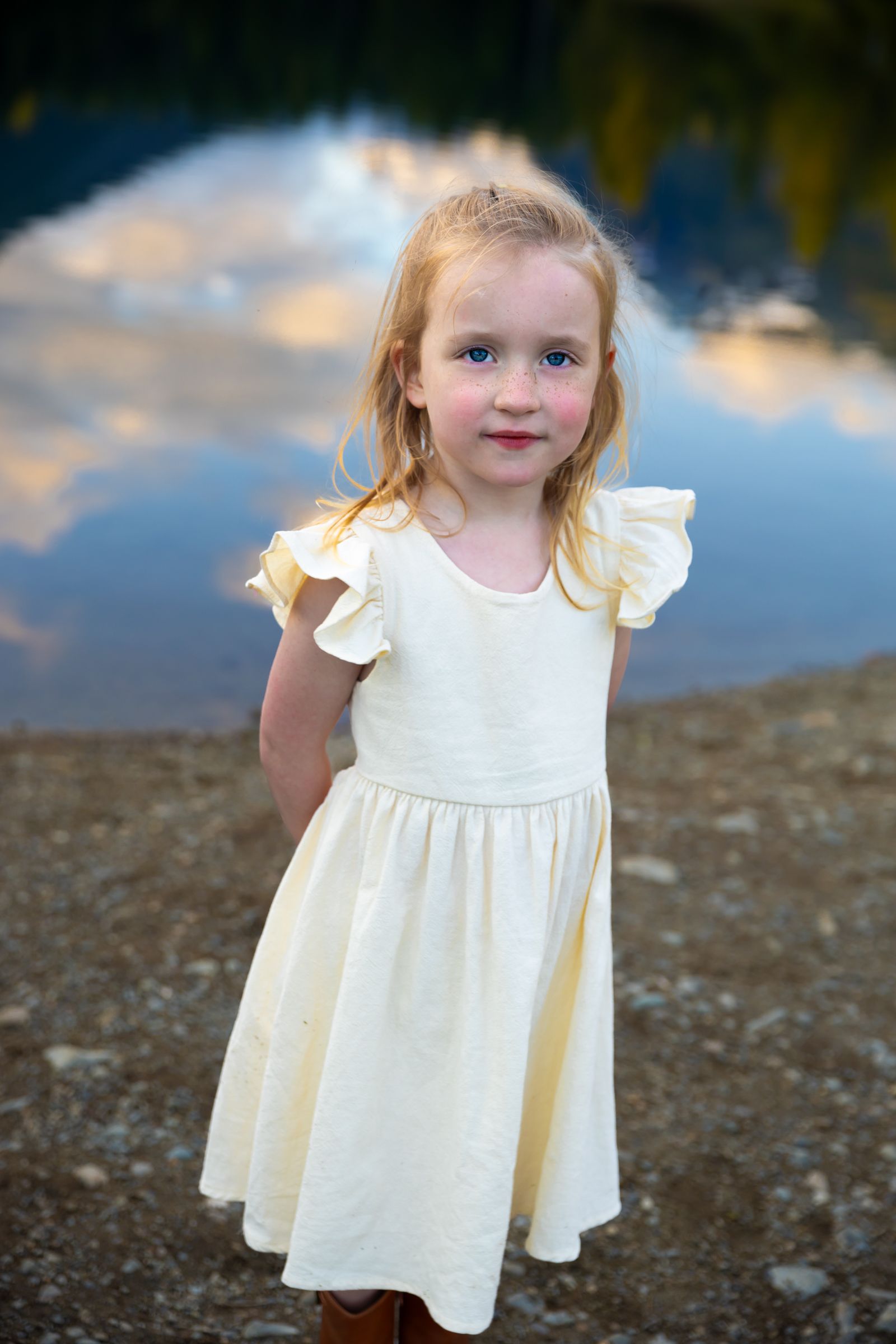 A young girl poses in front of a lake reflecting sunset clouds near Issaqua, Washington.