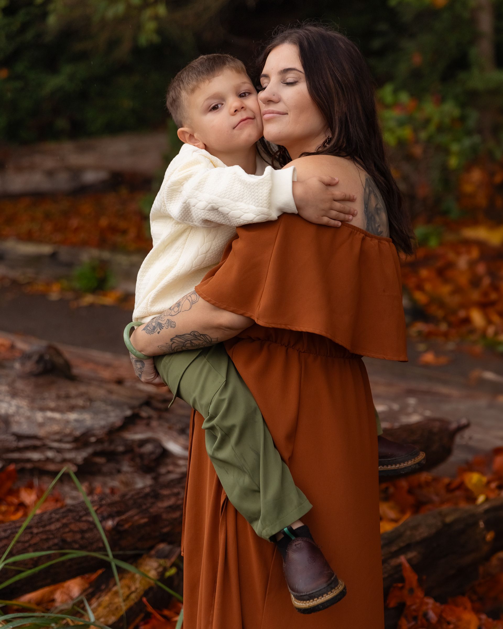 Jessica holds her son Jiovanni, surrounded by orange fall foliage, during a fall family session in Tacoma, Washington.