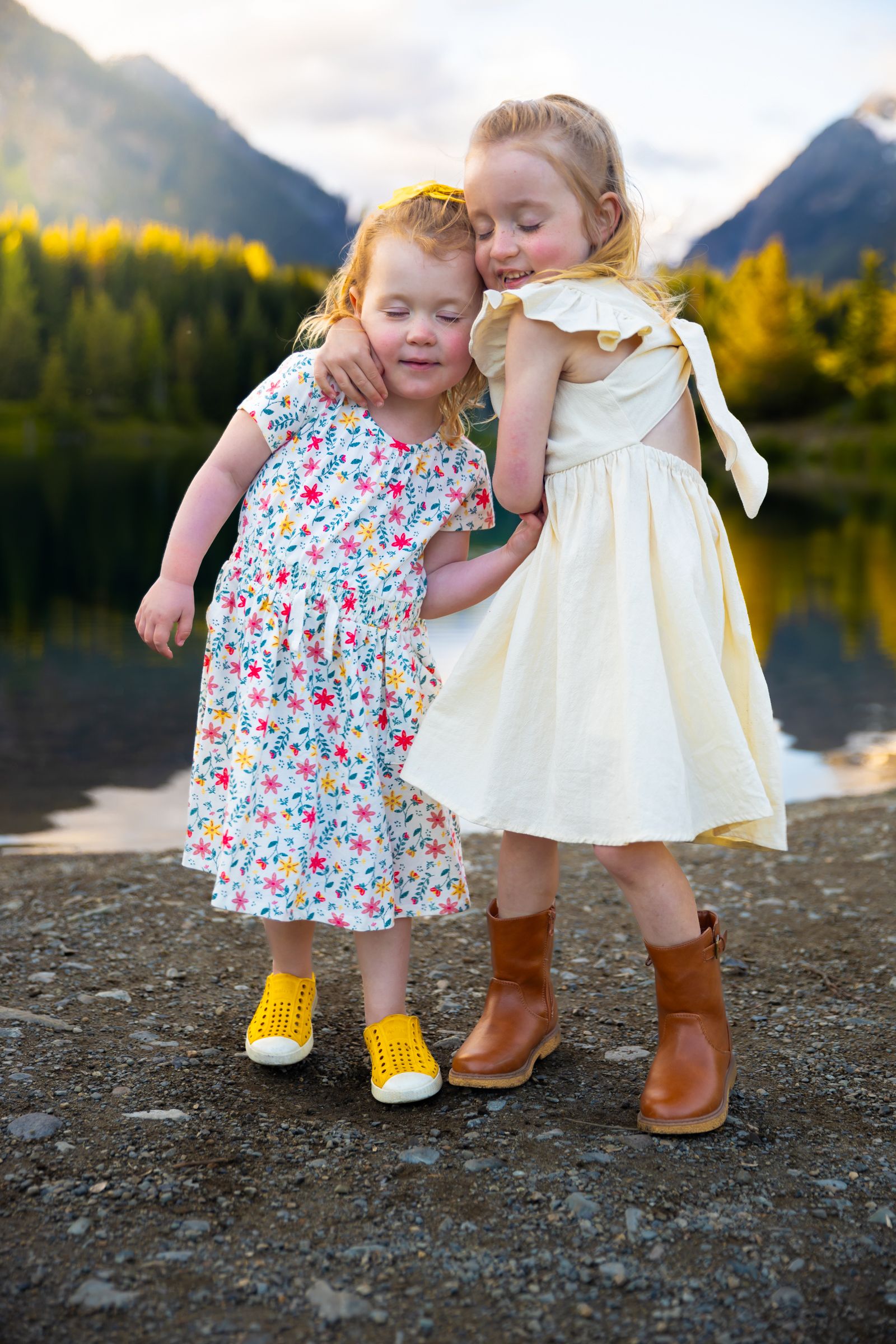 Young sisters hug in front of lake with a mountainous landscape in Snoqualmie, Washington.