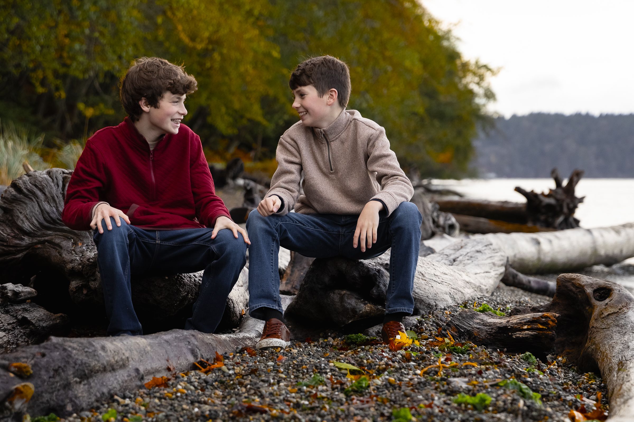 Tween brothers sit on large driftwood and chat during a family photography session at Owen Beach in Tacoma.